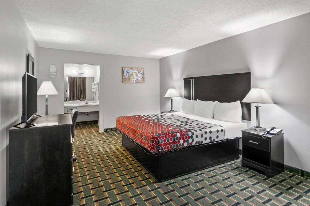 A hotel room with a bed, bedside tables, a desk, a mirror, and a patterned carpet.