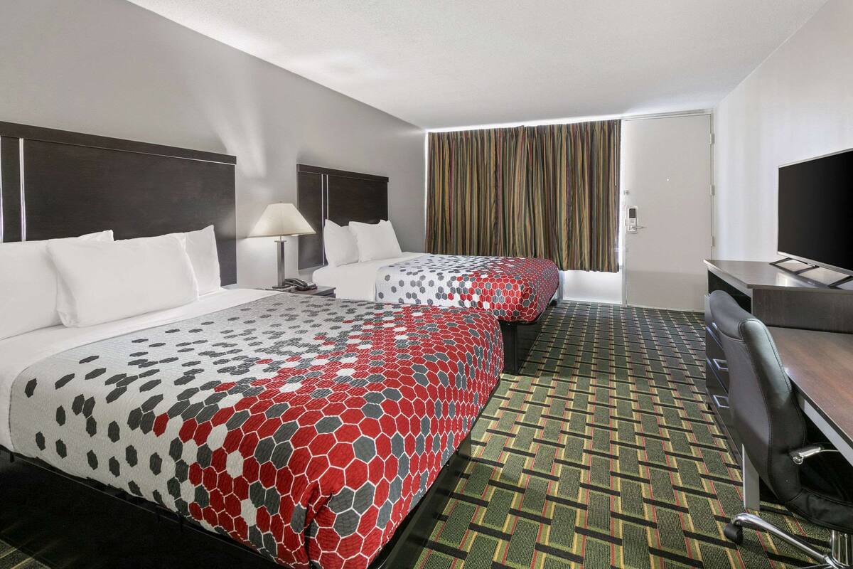 A hotel room with two beds, a desk, a chair, a TV, and a window with curtains.