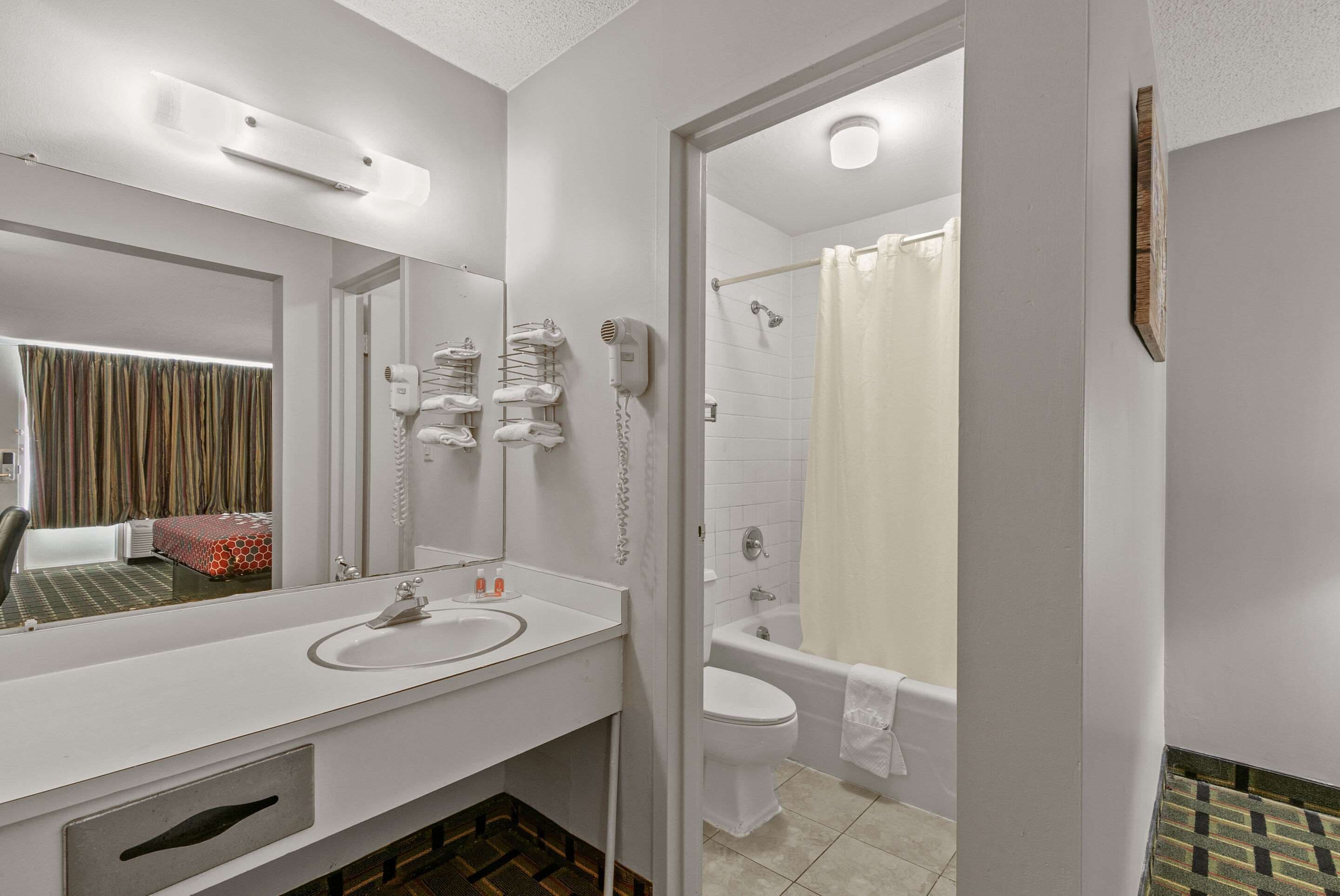 Baño de hotel con lavamanos, espejo, secador de pelo y zona de ducha.