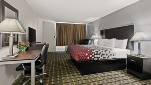 A hotel room with a bed, desk, chair, nightstand, lamp, and a view of the outside through curtains. - Econo Lodge Clemson - University Area (Clemson)