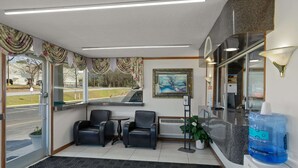 A reception area with a desk, two chairs, a large water dispenser, and a painting on the wall. - Econo Lodge Clemson - University Area (Clemson)