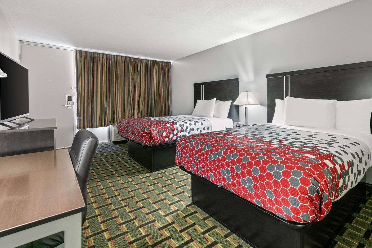 A hotel room with two beds, a desk, and a television.