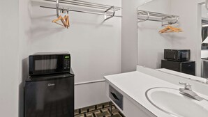 A compact bathroom with a white sink, a mirror, a black refrigerator, and a towel rack with wooden hangers. - Econo Lodge Clemson - University Area (Clemson)