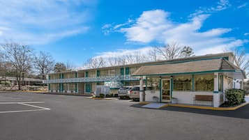 Un motel con una zona de estacionamiento techada, un pequeño espacio al aire libre para sentarse y una escalera que conduce a la entrada.