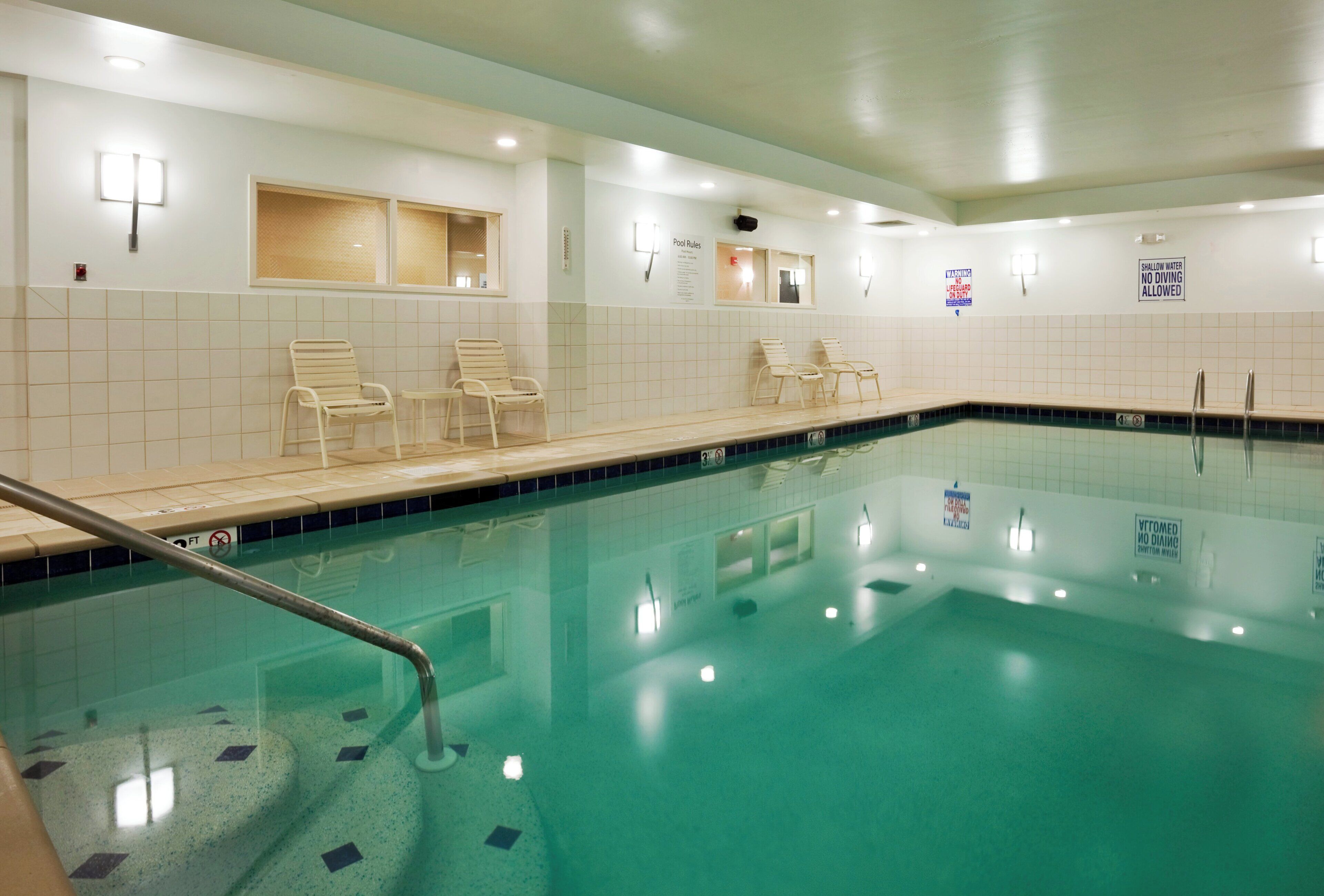 An indoor swimming pool with clear water, a diving board, and lounge chairs along the edge.