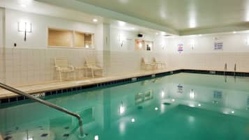 An indoor swimming pool with clear water, a diving board, and lounge chairs along the edge.