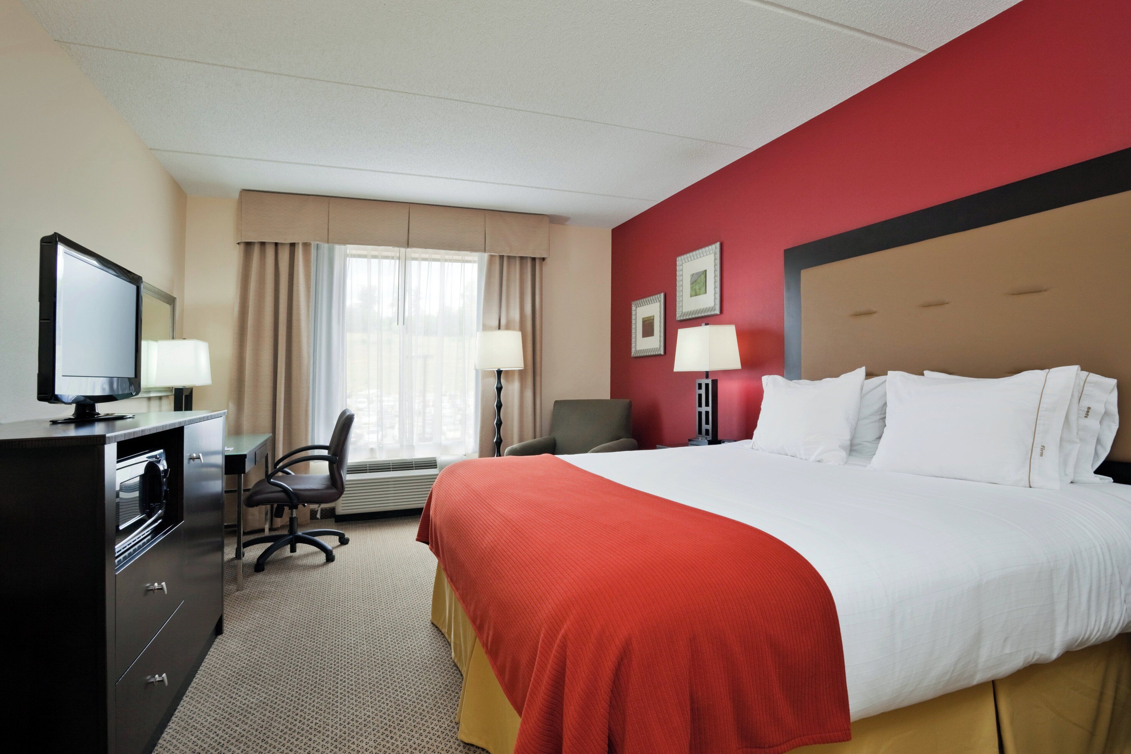 A hotel room with a bed, desk, chair, television, and two lamps.