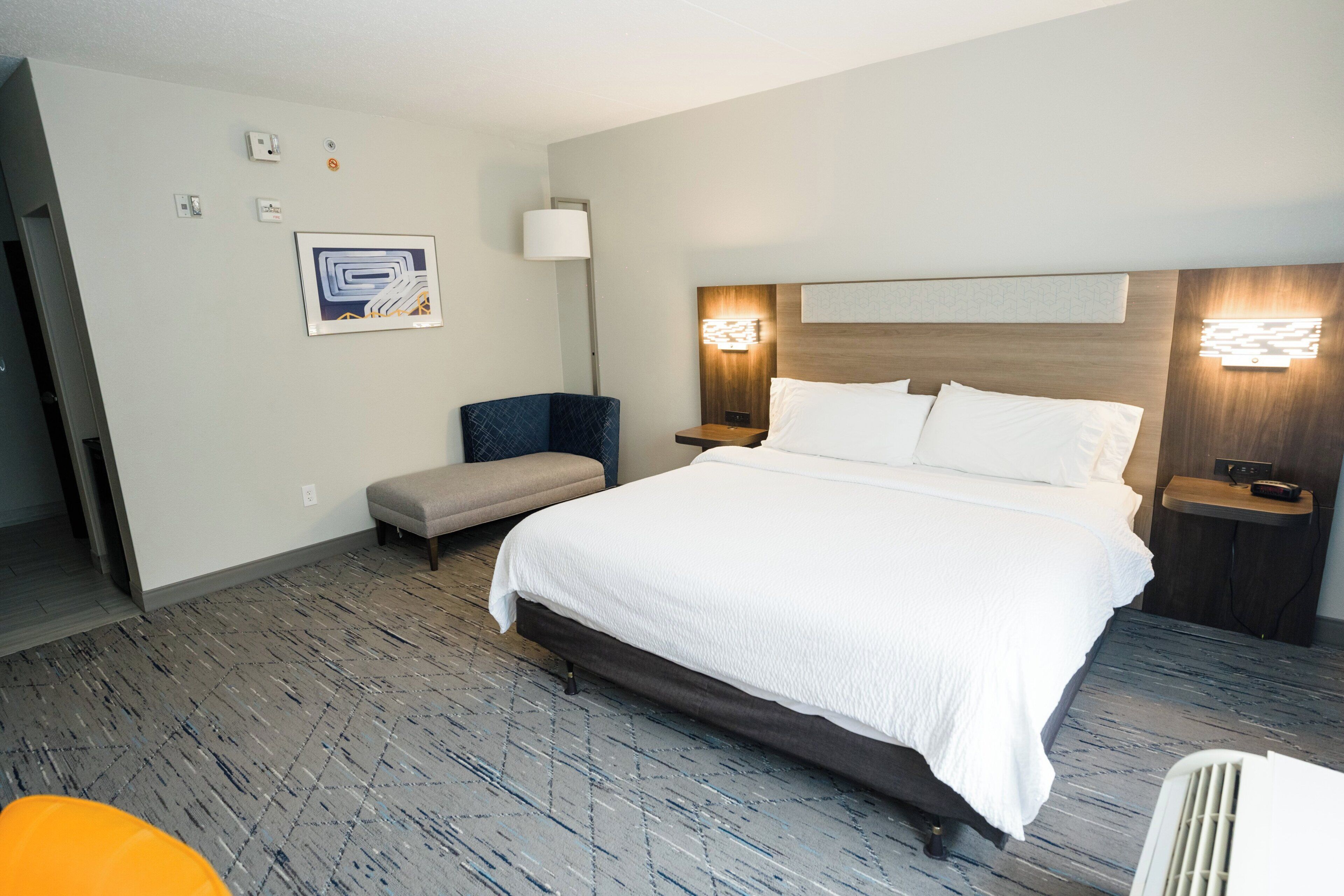 Een hotelkamer met een groot bed, een stoel, een nachtkastje en een wandlamp.