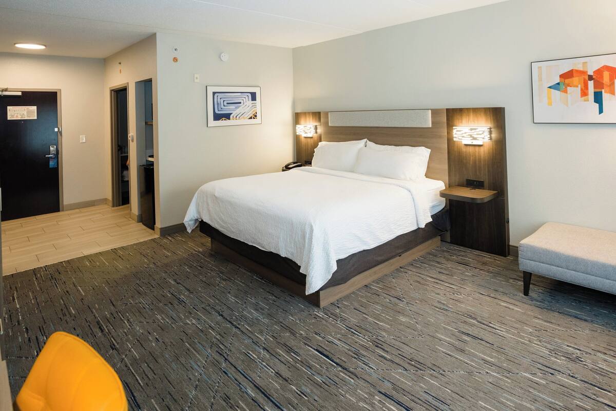 Una camera d'albergo con un letto grande, comodini, una sedia e un pavimento in legno.