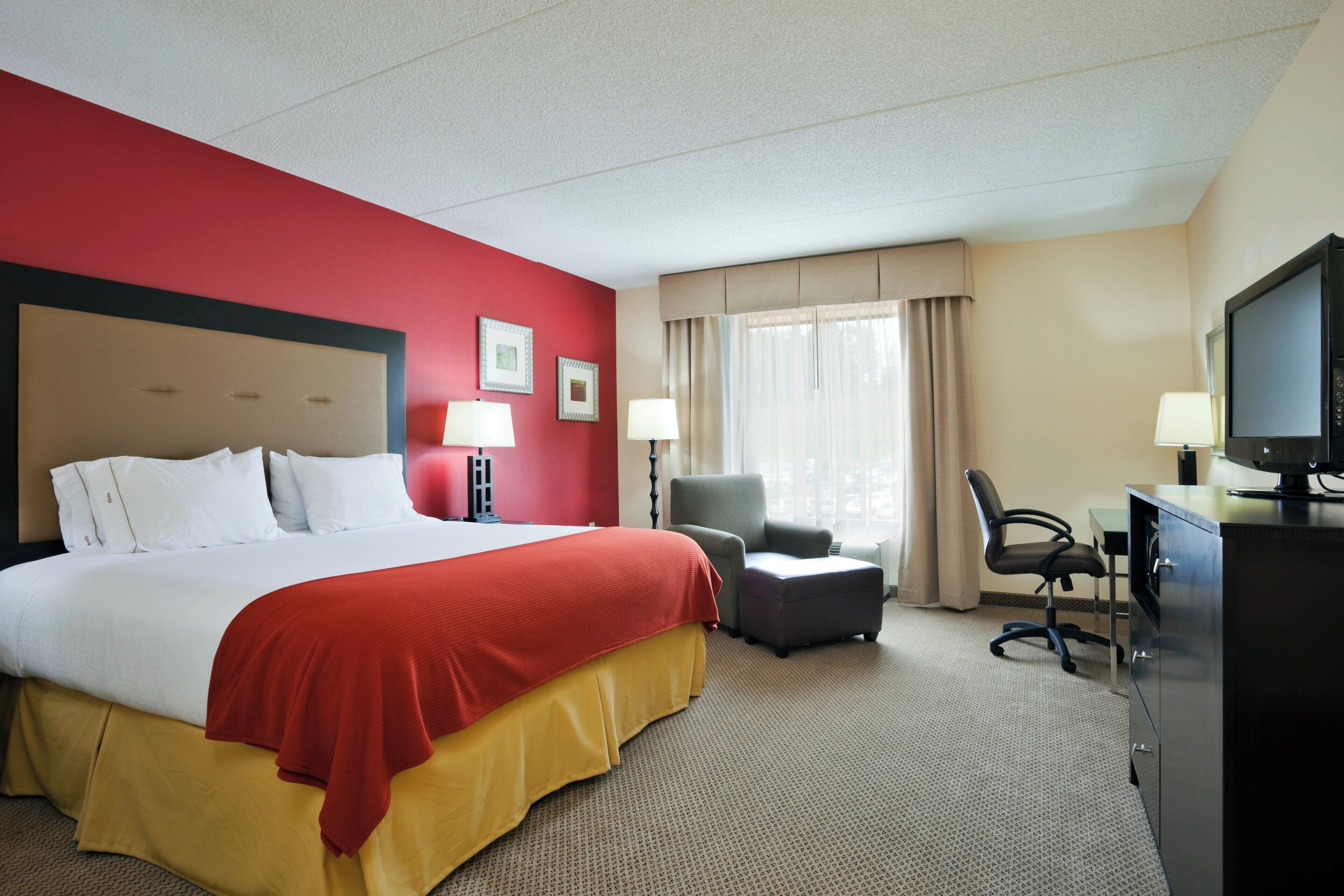Une chambre d’hôtel avec un grand lit, un bureau, une chaise, une télévision et deux lampes.