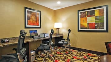 Une chambre d’hôtel équipée d’un bureau, de deux chaises, d’un ordinateur, d’un téléphone et de deux œuvres d’art encadrées accrochées aux murs.
