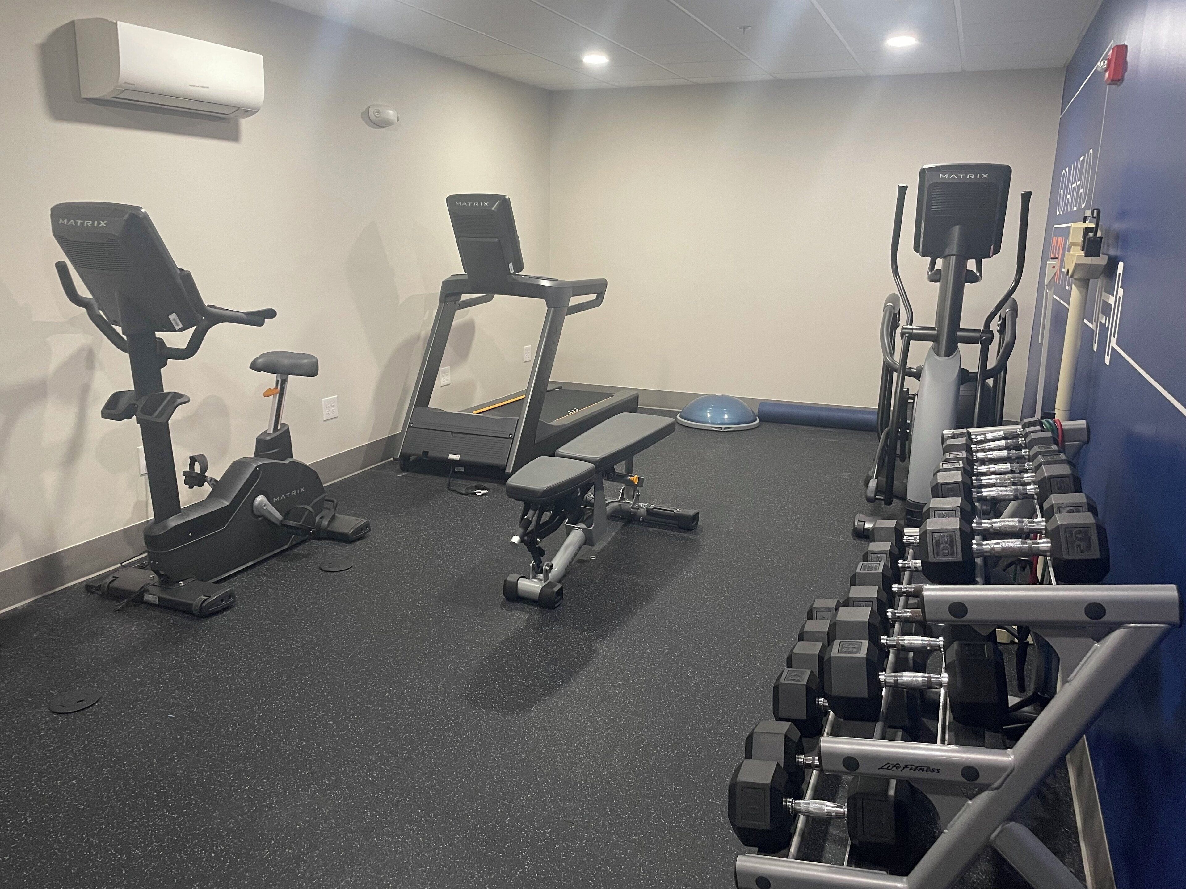 A gym with various exercise equipment including treadmills, an elliptical, and dumbbells.