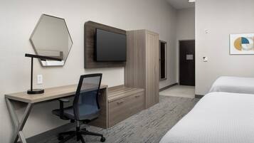 A hotel room with a desk, chair, bed, wardrobe, television, and artwork on the wall.