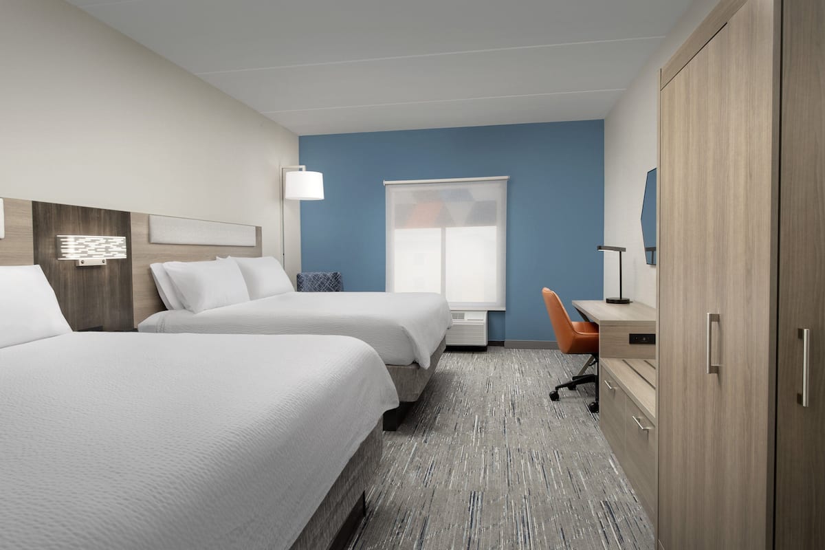 A hotel room with two beds, a desk, a chair, and a wardrobe.