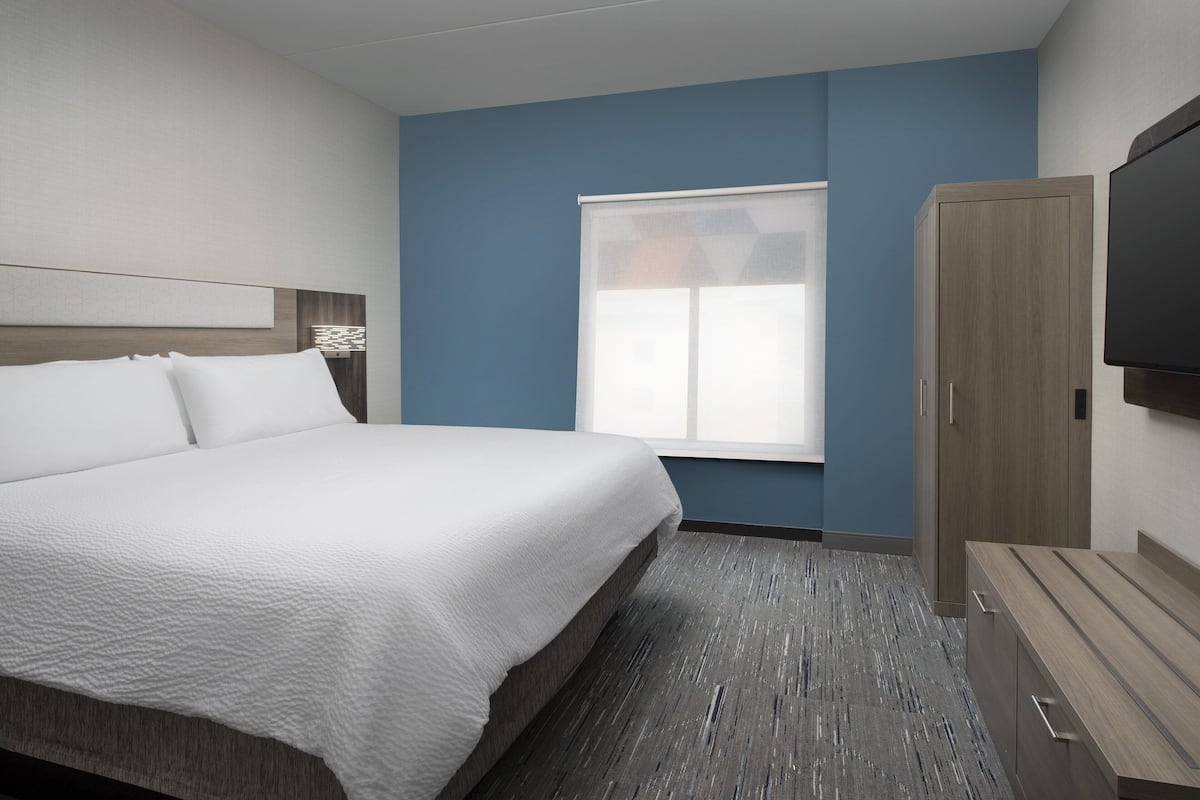A hotel room with a large bed, a wooden wardrobe, a flat-screen TV, and a window with blinds.