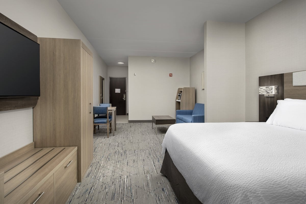 A hotel room with a large bed, a desk, a chair, a wardrobe, and a flat-screen TV.
