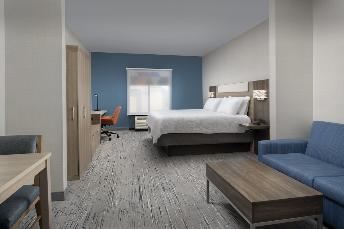 A hotel room with a bed, a desk, a chair, a sofa, and a window.