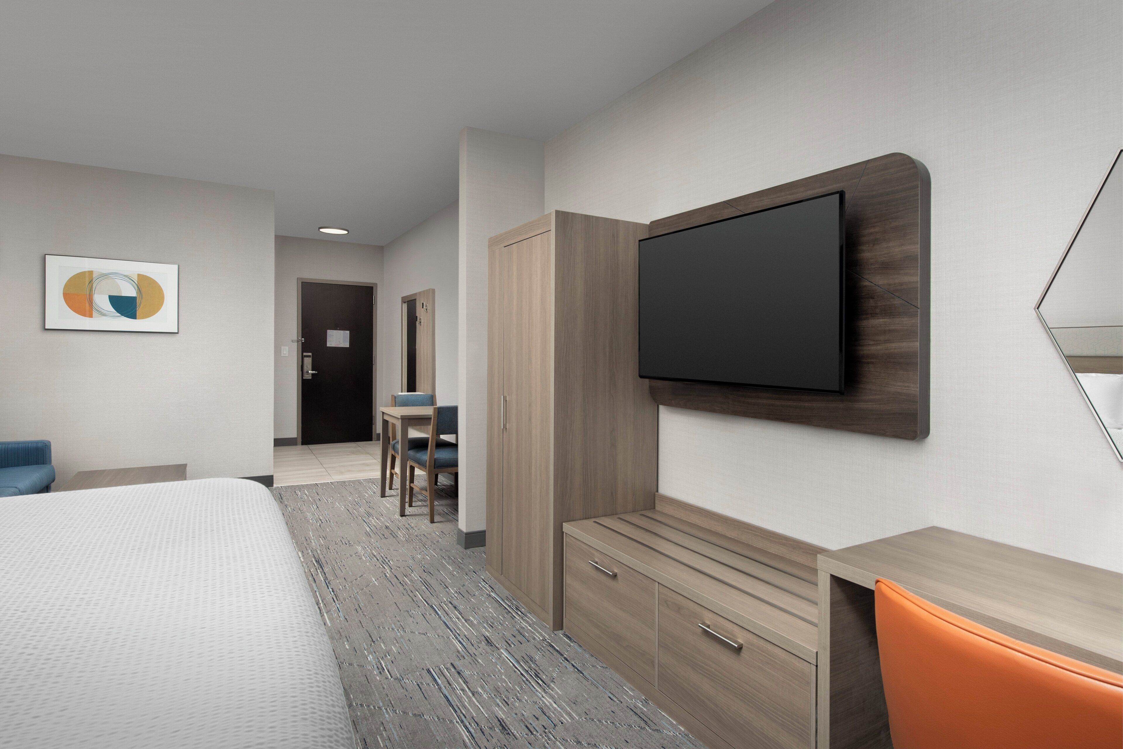 Una habitación de hotel con una cama, un escritorio, una silla, un televisor montado en la pared y un cuadro en la pared.