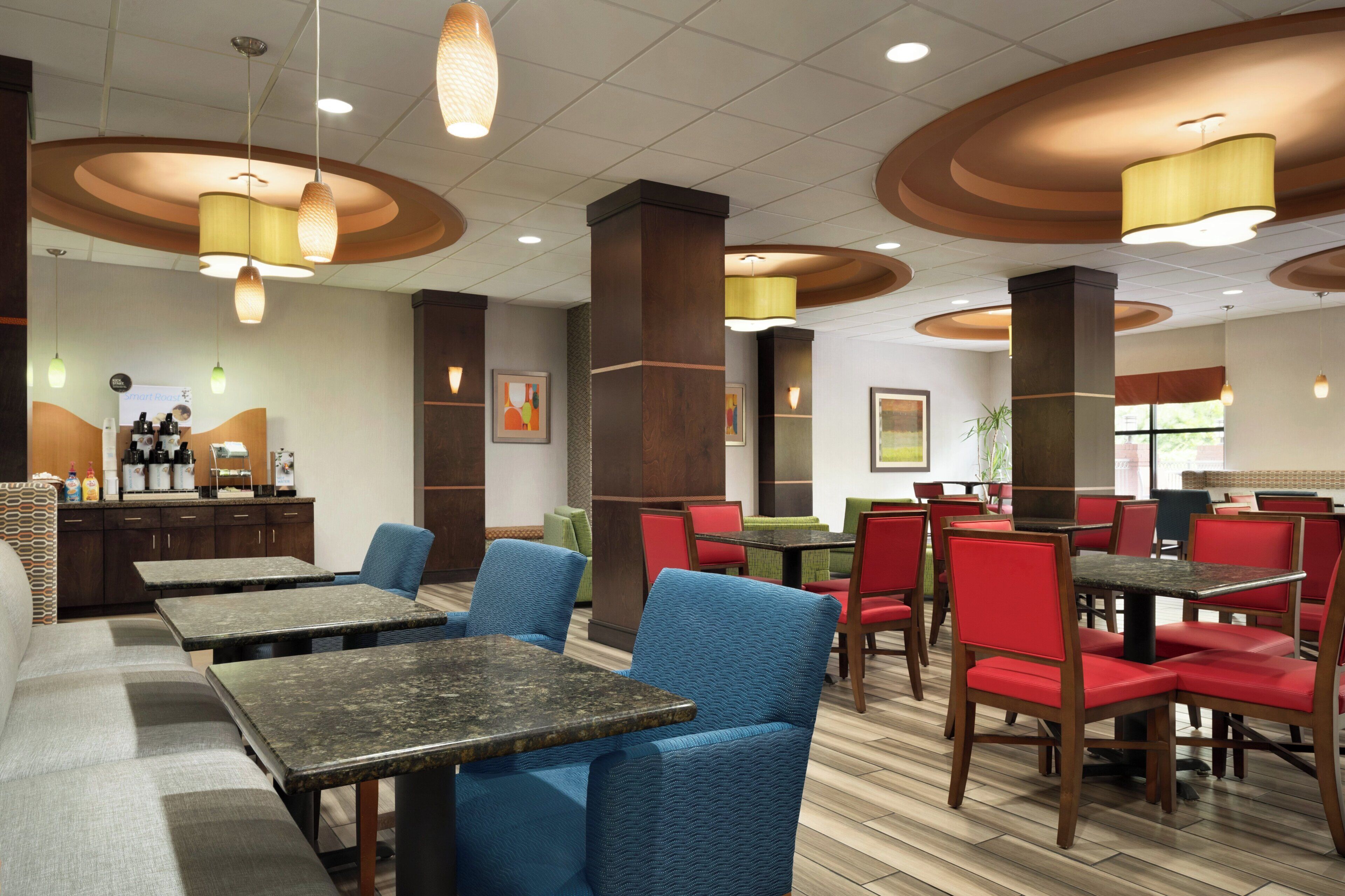A hotel dining area with multiple tables and chairs, a coffee station, and artwork on the walls.