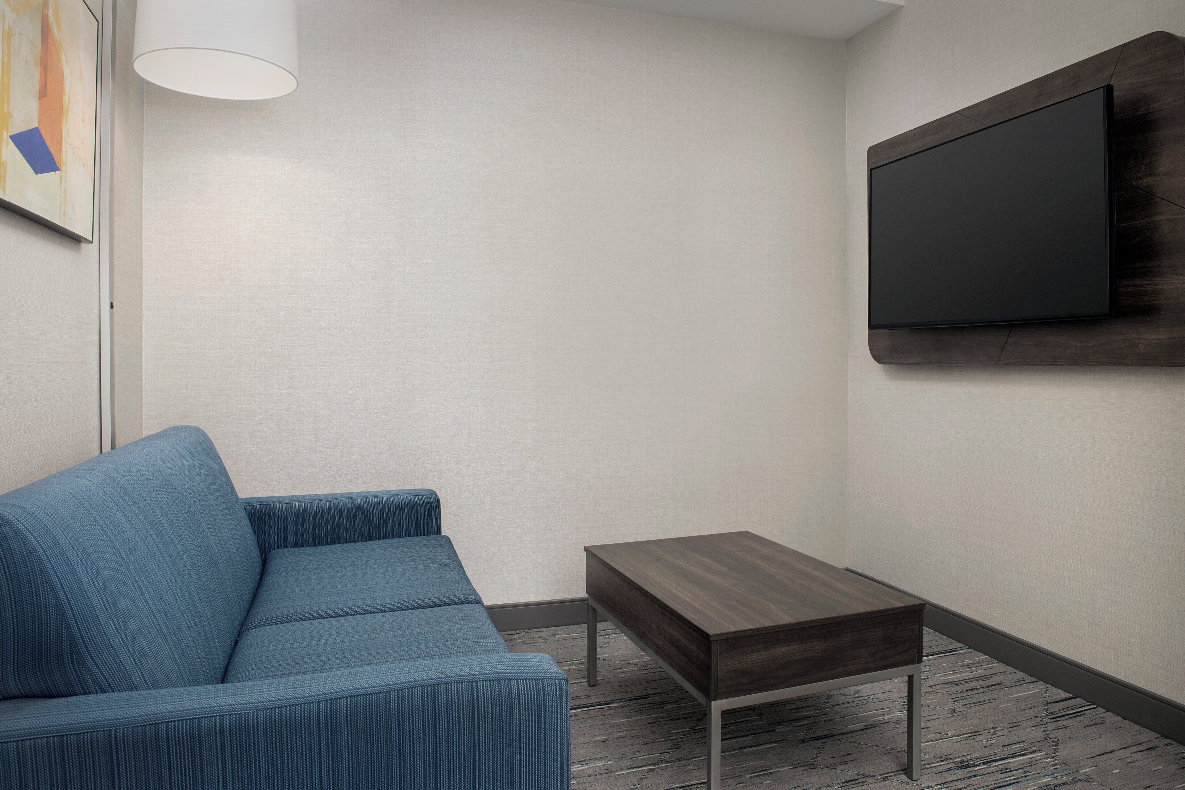 Un saló modern amb un sofà blau, una taula de fusta petita i un televisor penjat a la paret.