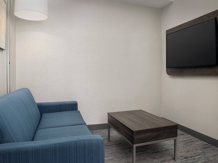 A modern living room with a blue sofa, a small wooden table, and a mounted TV on the wall.
