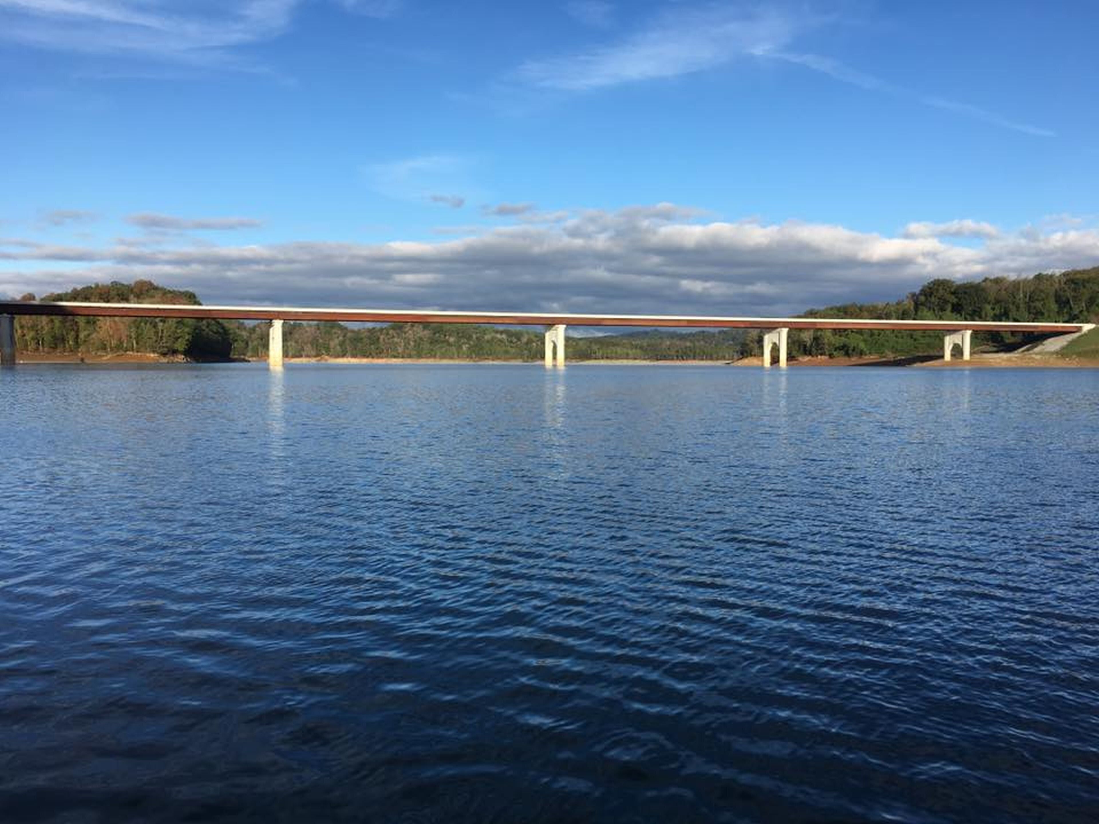 Un puente sobre un cuerpo de agua, con cielo despejado y árboles distantes.