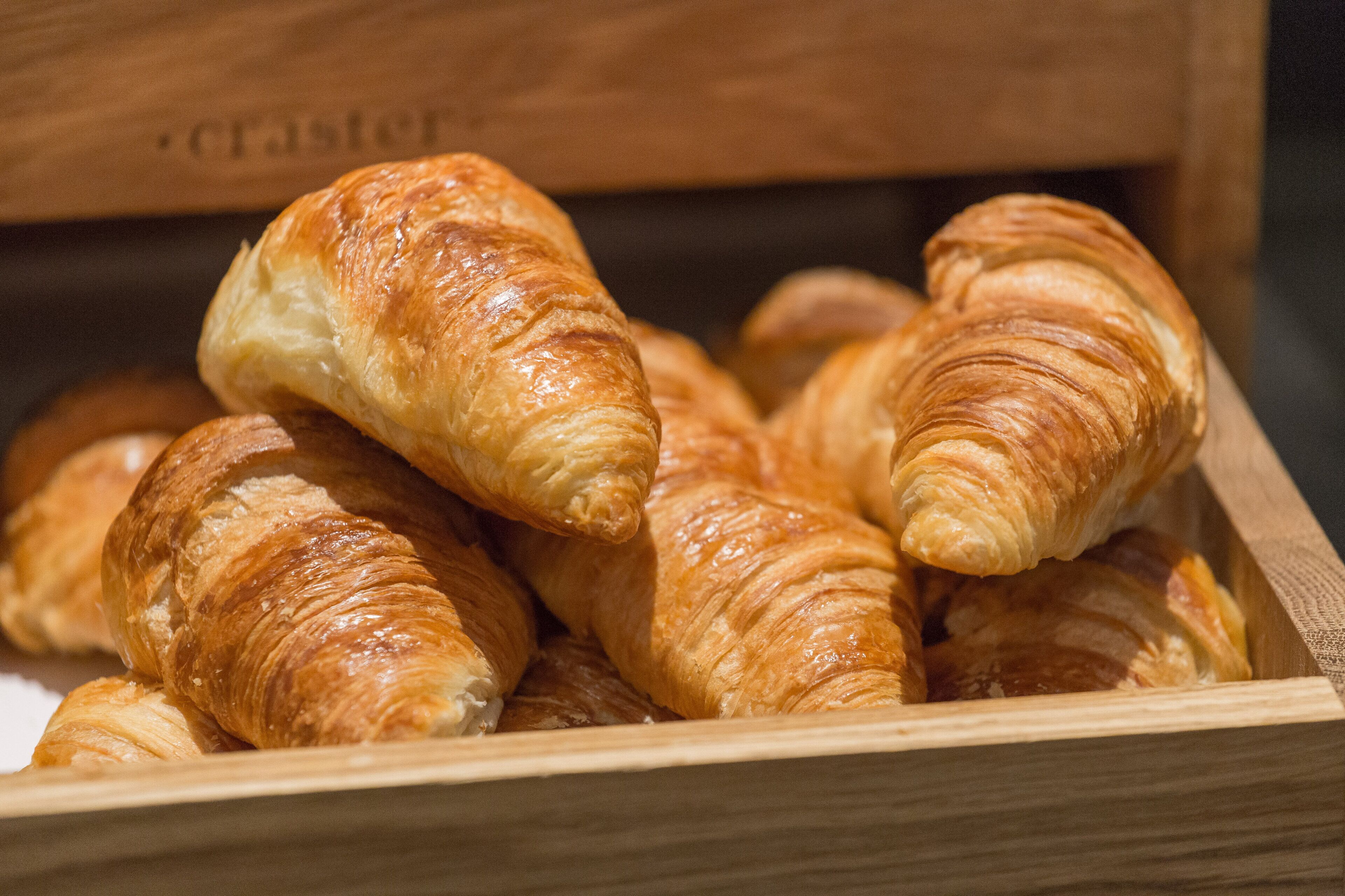 Una caja de madera con varios croissants dorados y tostados.