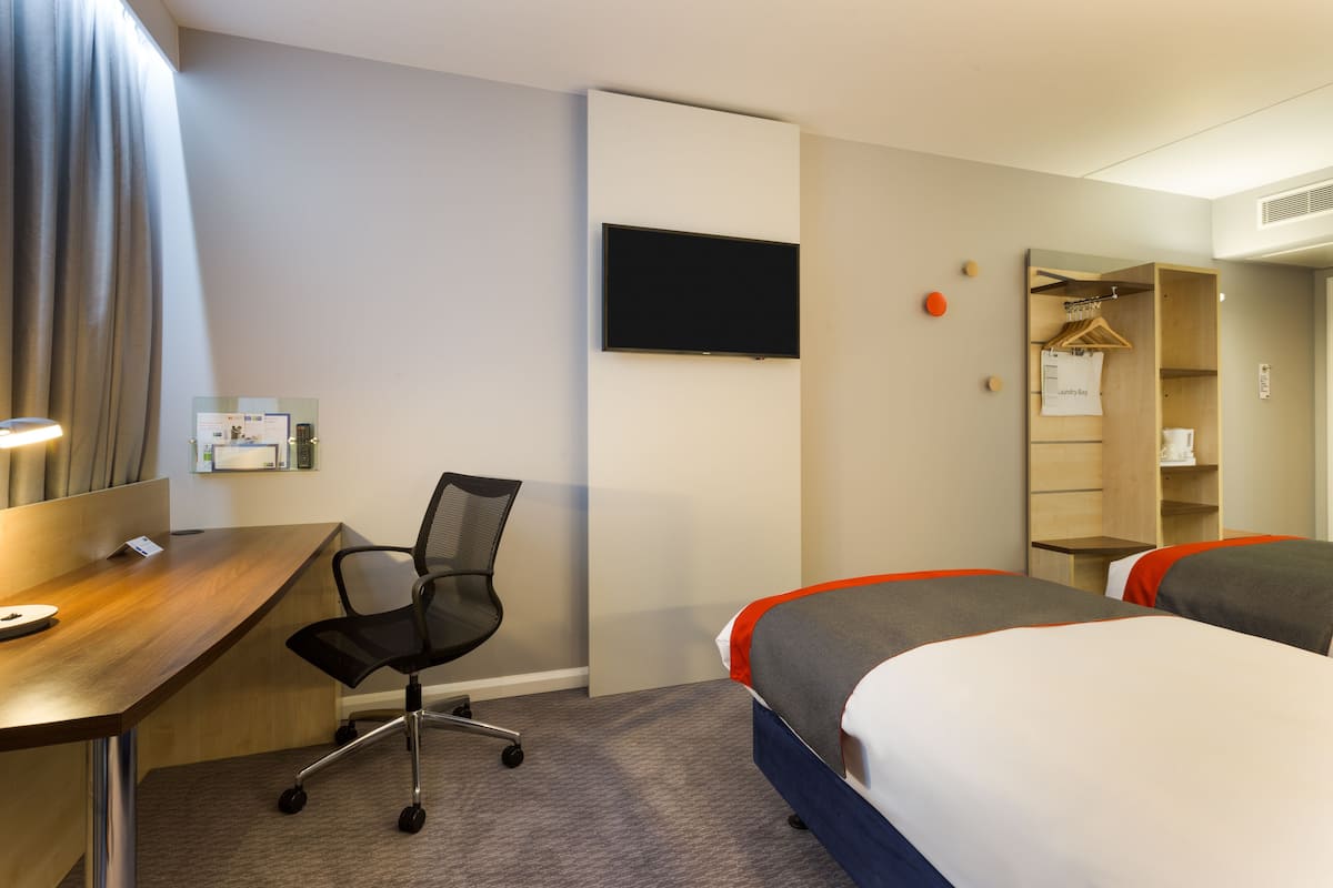 A hotel room with a desk, two beds, a TV, a coat rack, and a wardrobe.