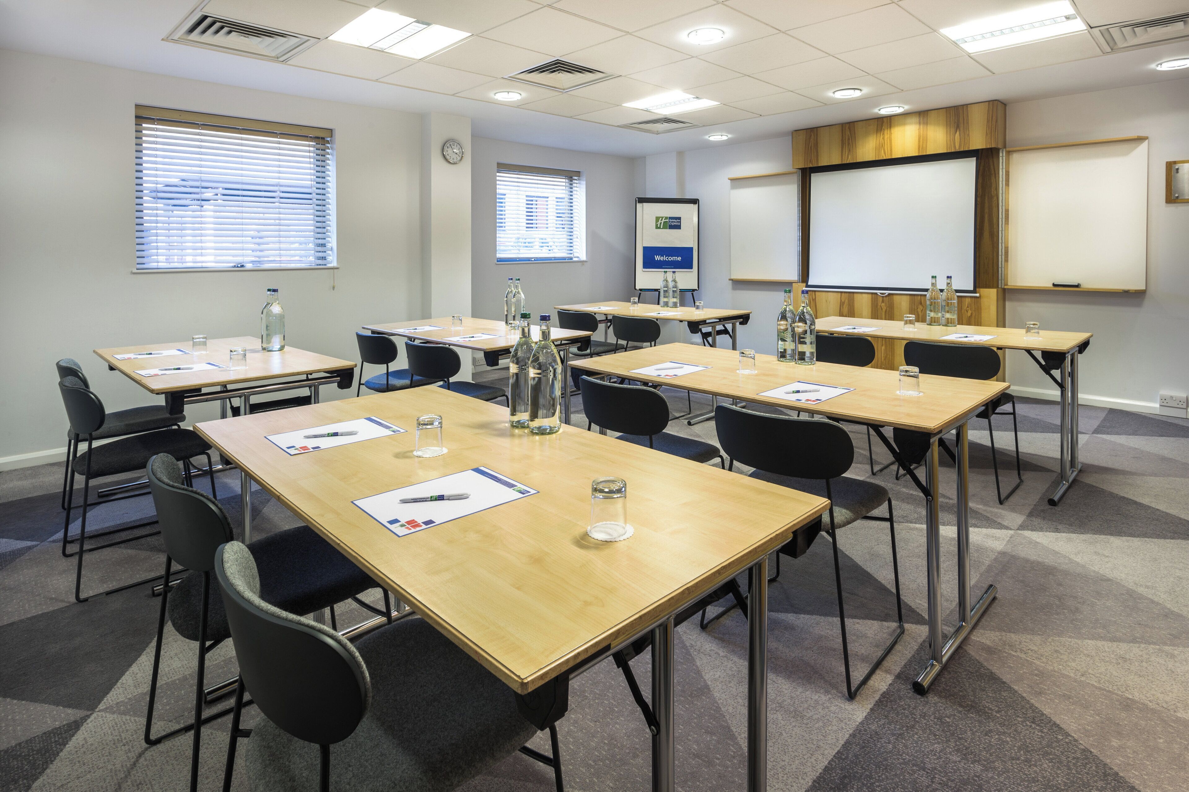 Une salle de conférence équipée de plusieurs tables, de chaises et d’écrans de présentation.