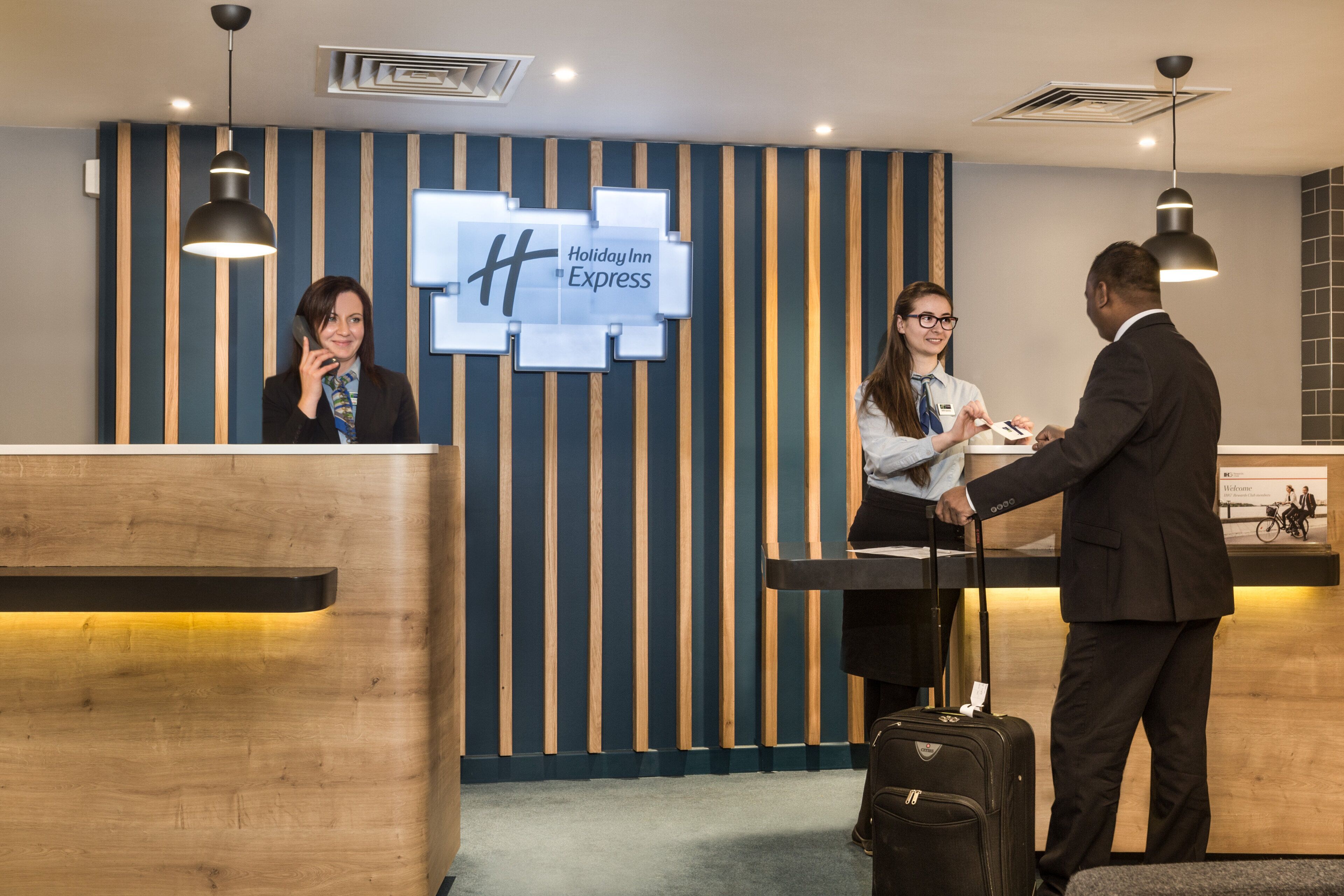 A reception desk with a Holiday Inn Express sign, a wooden panel wall, and a luggage trolley.
