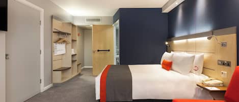 A hotel room with a bed, a bedside table with a phone, a red chair, a wardrobe, and a television on the wall.