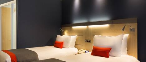 Ein Hotelzimmer mit zwei Betten, jeweils mit weißer Bettwäsche und roten Akzenten, einem Holz-Kopfteil und einer Nachttischlampe.