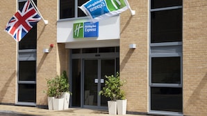 Un bâtiment de l’hôtel Holiday Inn Express avec une façade en briques, deux plantes en pot devant l’entrée et des drapeaux, dont le drapeau du Royaume-Uni.