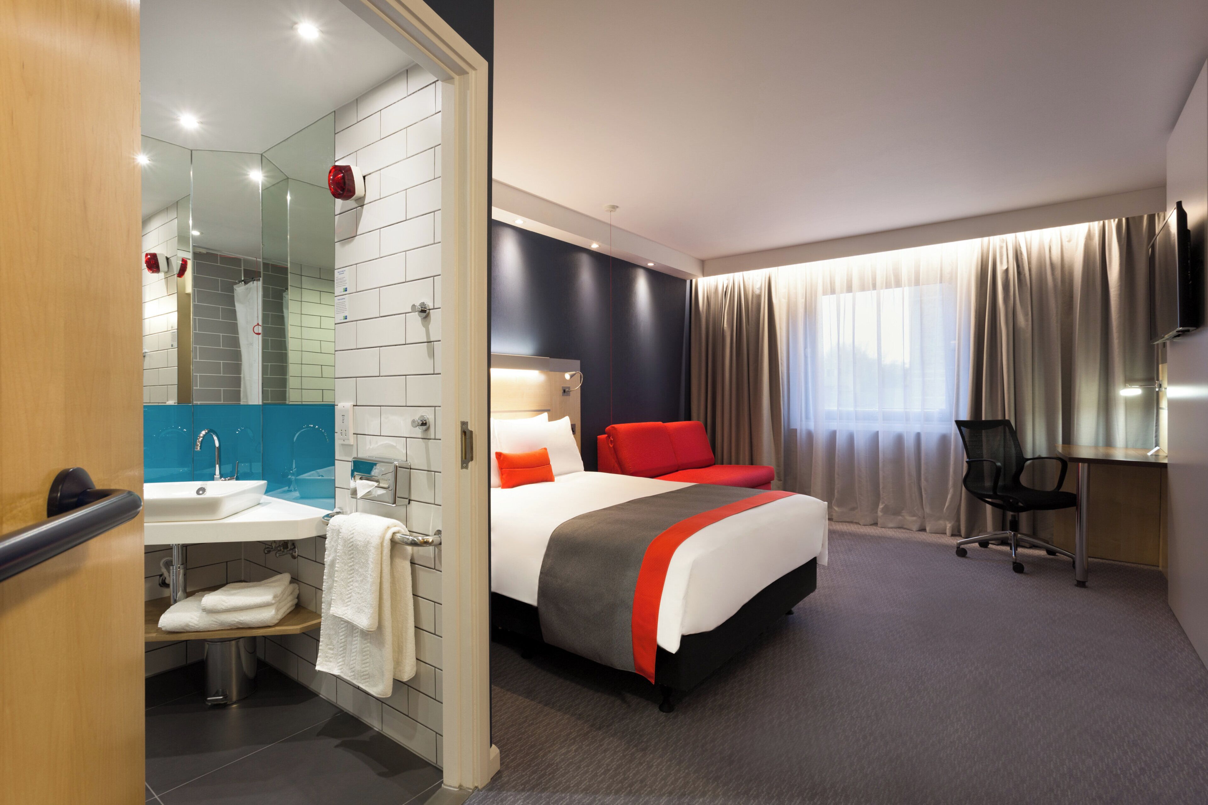 A hotel room with a bed, a bathroom with a sink, and a TV mounted on the wall.