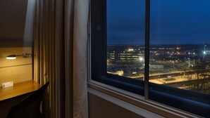 Ein Hotelzimmer mit großem Fenster mit Blick auf eine beleuchtete Stadtlandschaft bei Nacht.