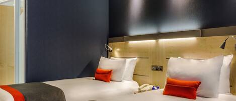 A hotel room with two beds, a wooden headboard, a bedside table with a lamp, and a phone.