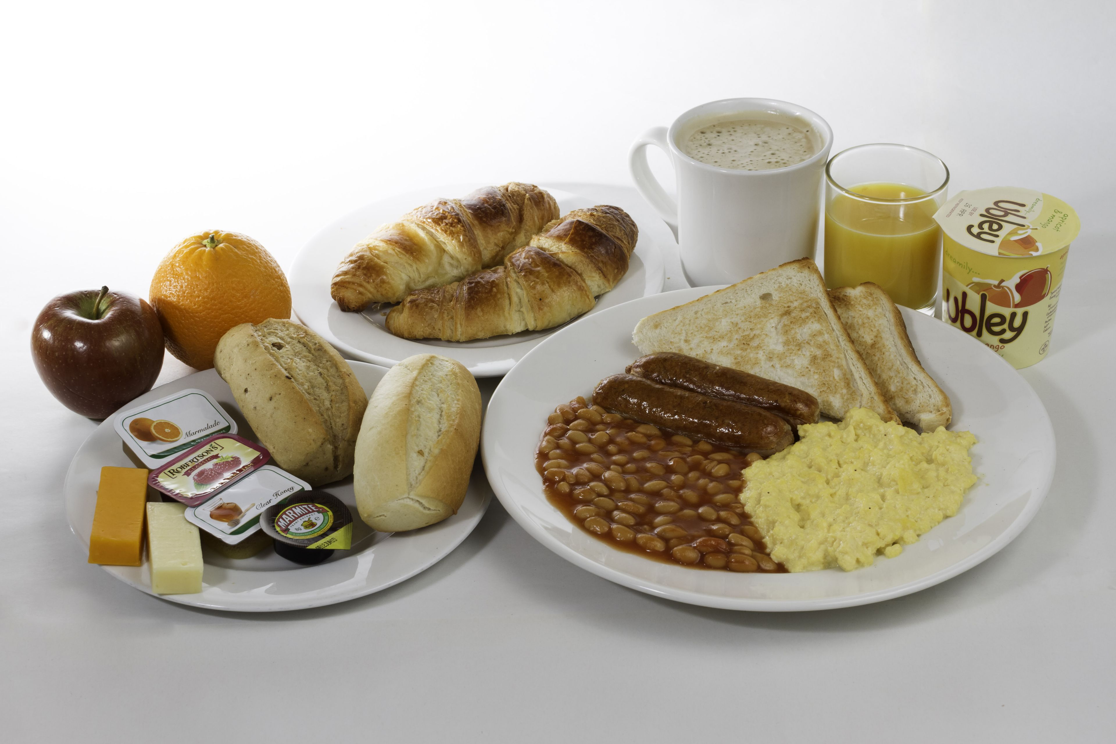 A breakfast plate with toast, beans, scrambled eggs, sausages, an apple, an orange, a croissant, a muffin, and a cup of coffee.