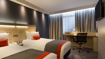 Habitación de hotel con dos camas, un escritorio, una silla y un televisor.