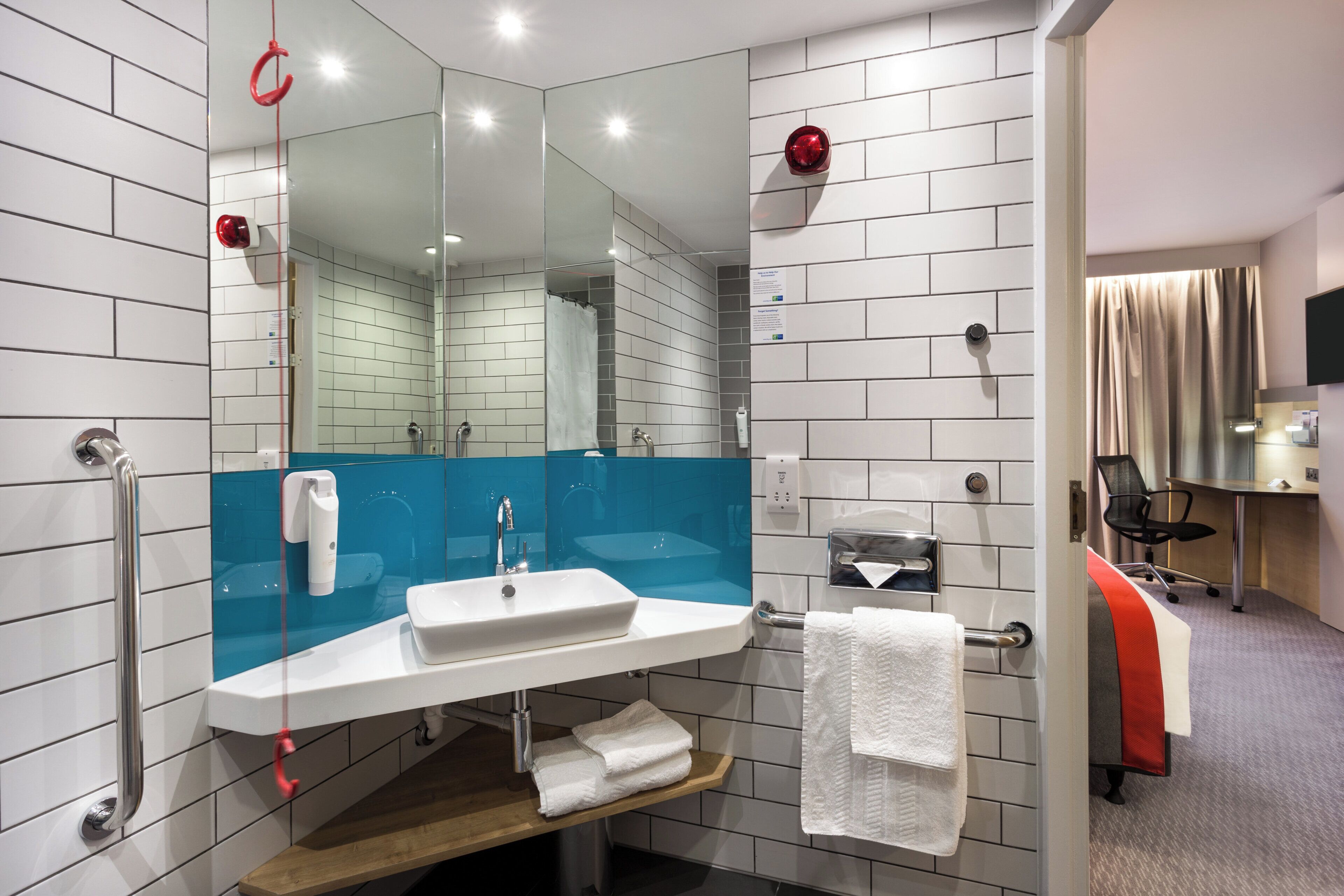 Un baño moderno con un lavabo blanco, un espejo, cabina de ducha de vidrio y un estante de madera.