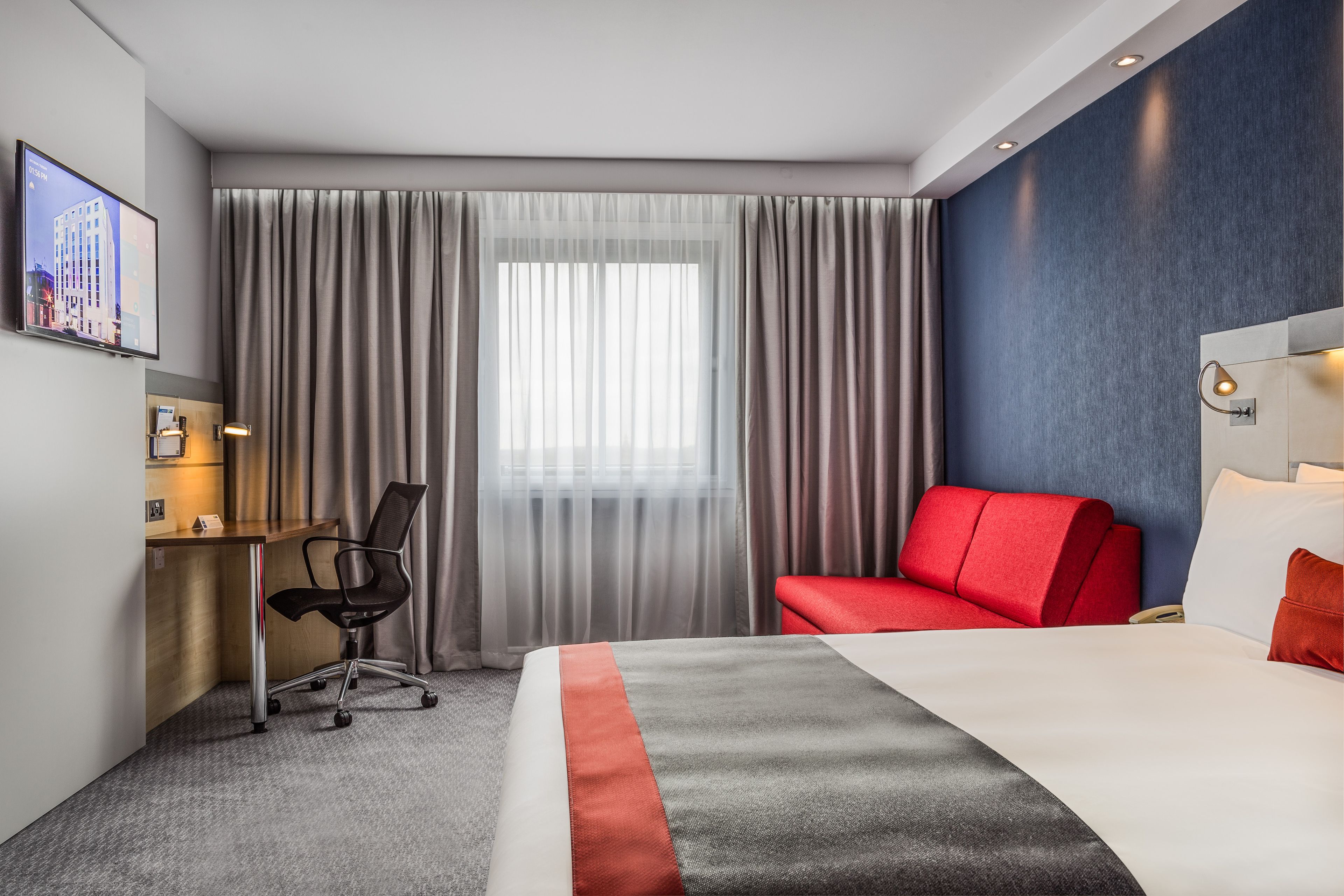 Una habitación de hotel con una cama, un escritorio, una silla y un sofá rojo.