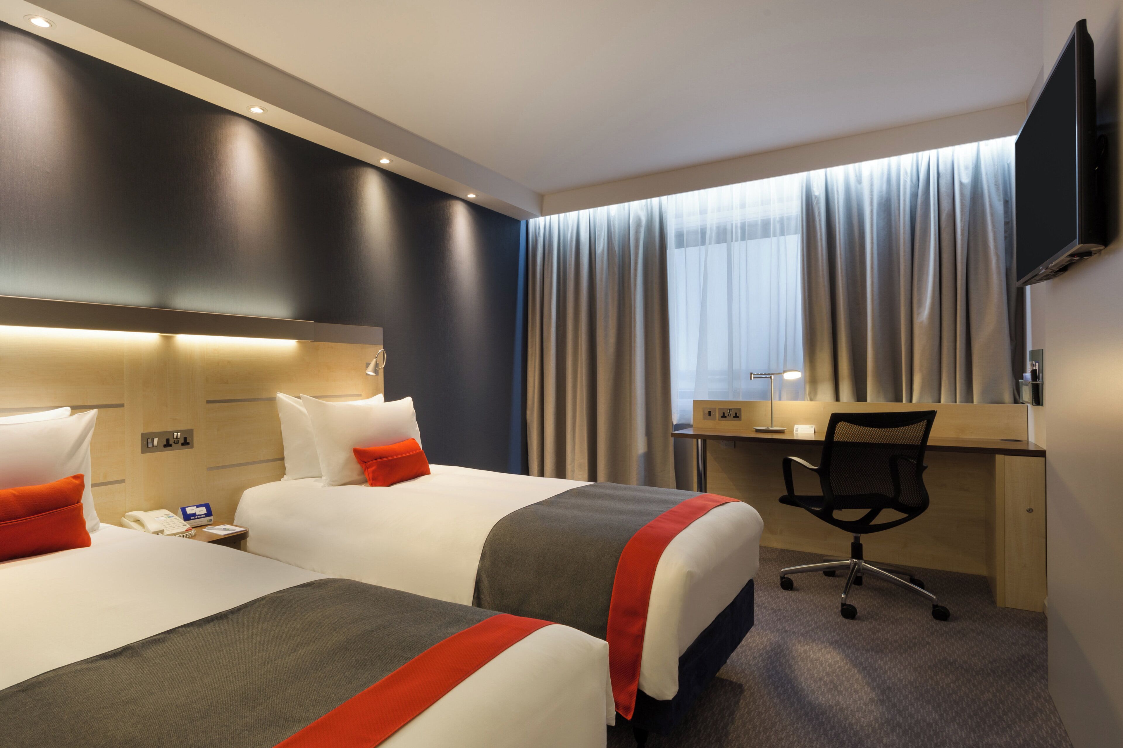 Habitación de hotel con dos camas, un escritorio, una silla, un televisor y una ventana con cortinas.