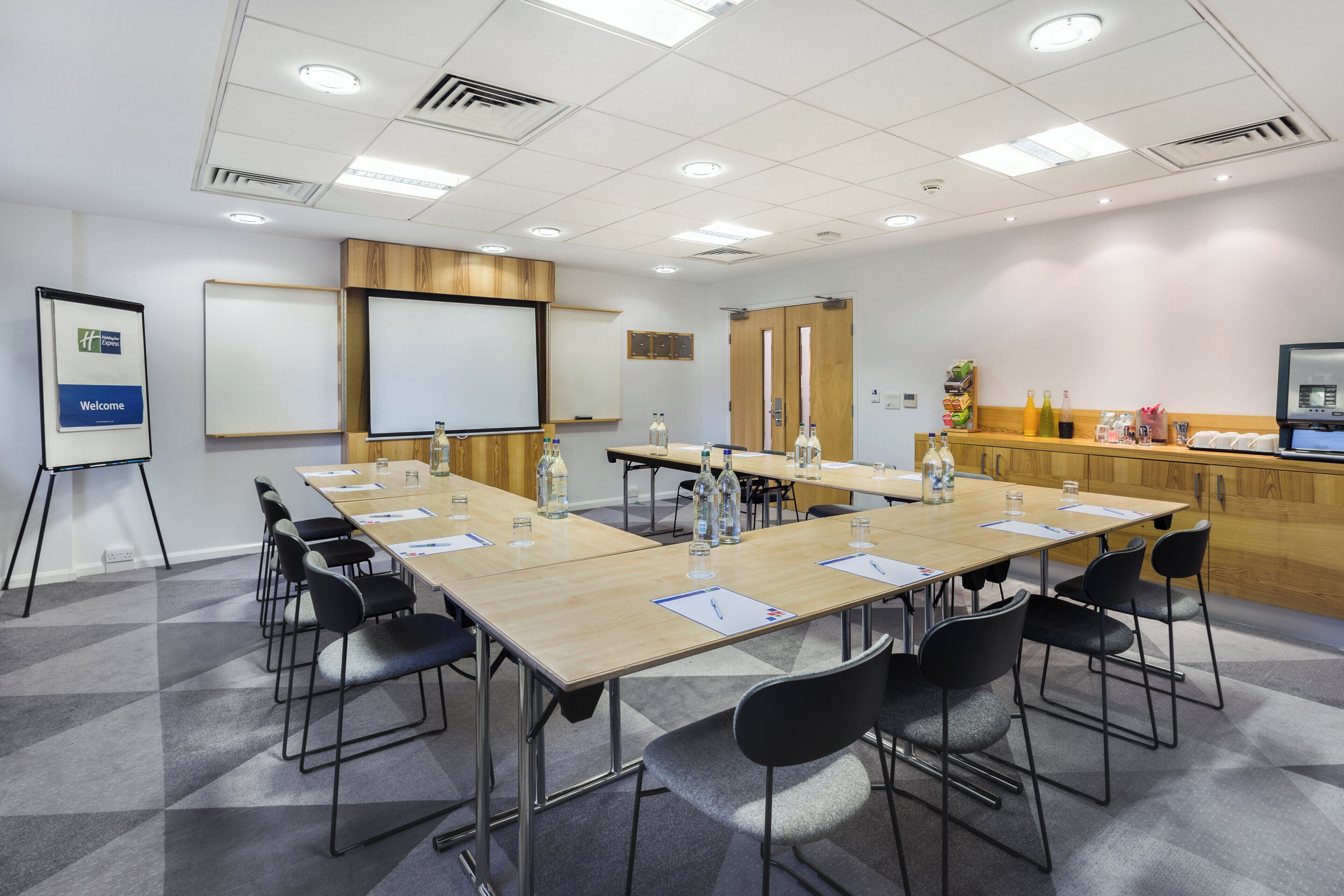 A conference room with a long table, chairs, a projector screen, and a whiteboard.