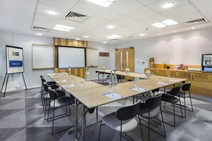 A conference room with a long table, chairs, a projector screen, and a whiteboard. - Holiday Inn Express London-Watford Junction by IHG (Watford)