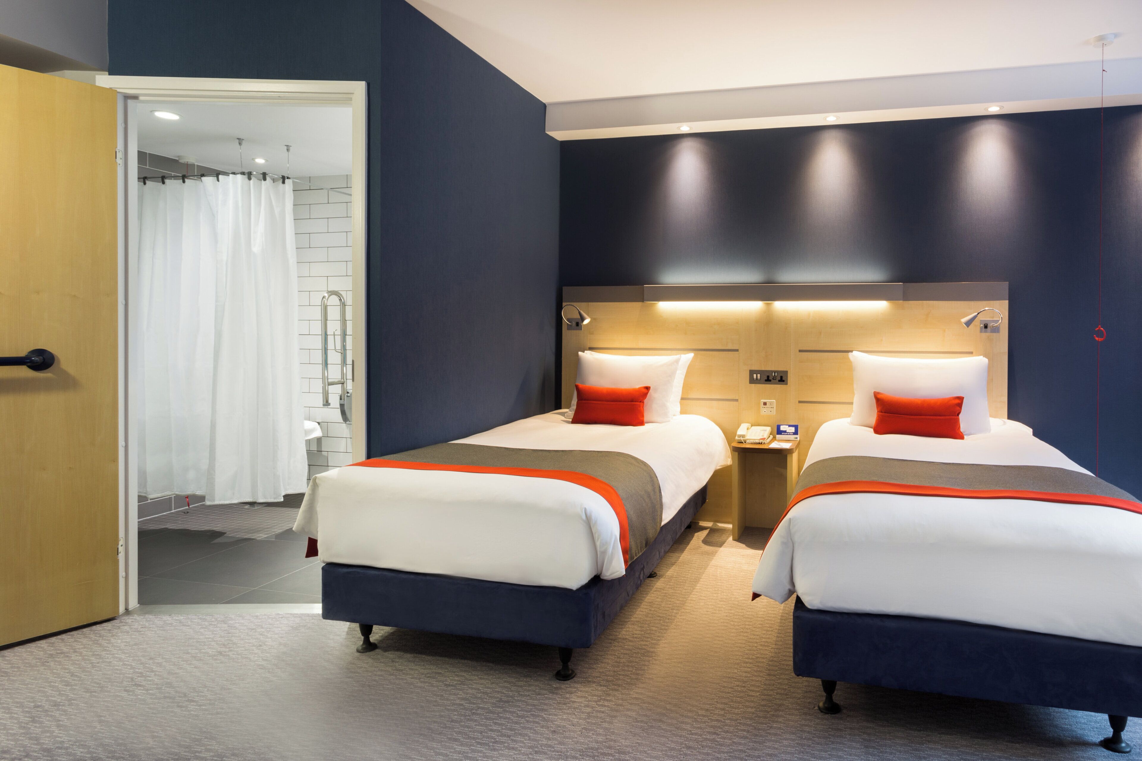 A hotel room with two beds, a bathroom, and a door.