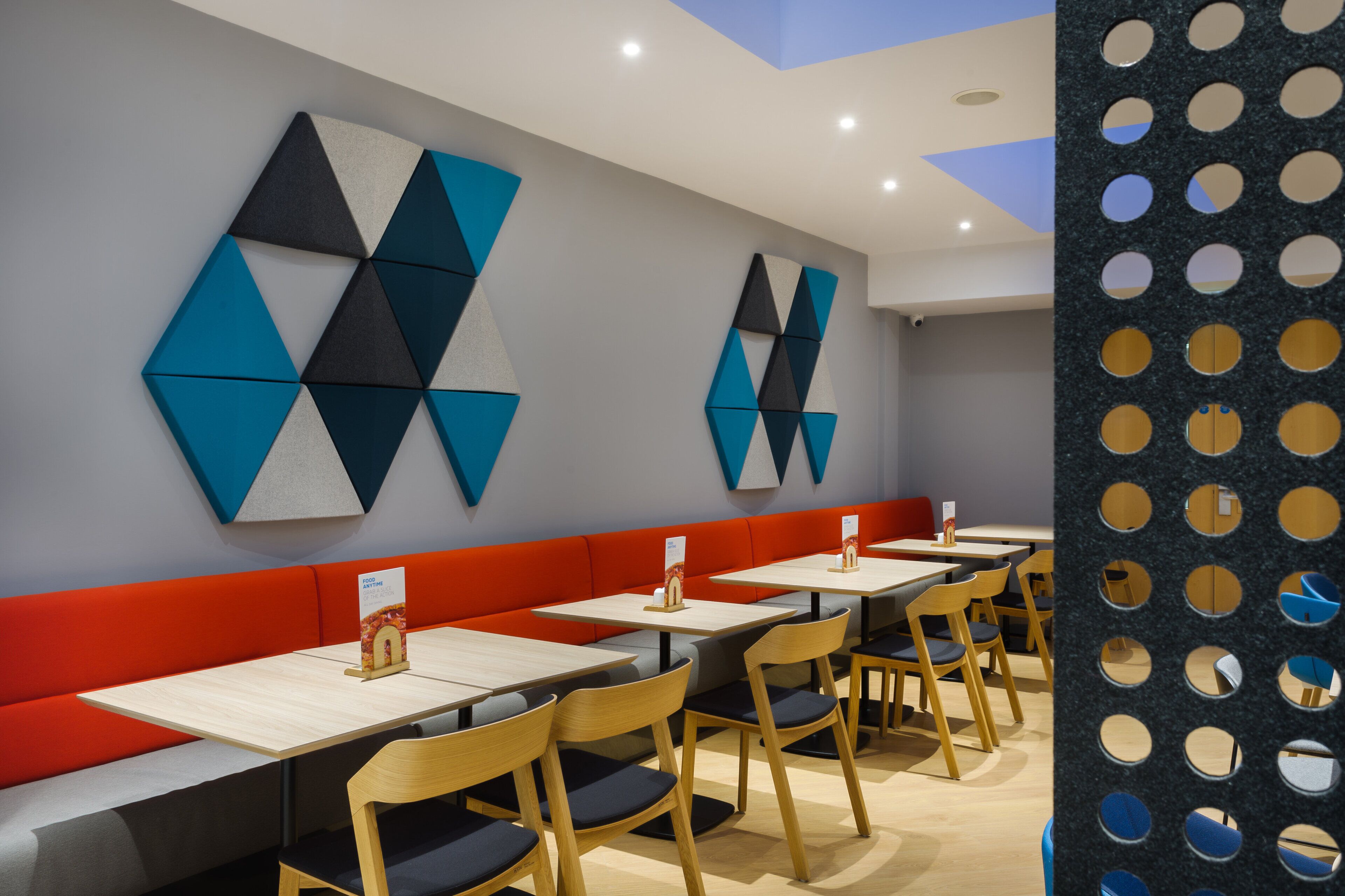 A modern restaurant interior with geometric wall art, red seating, and wooden tables.