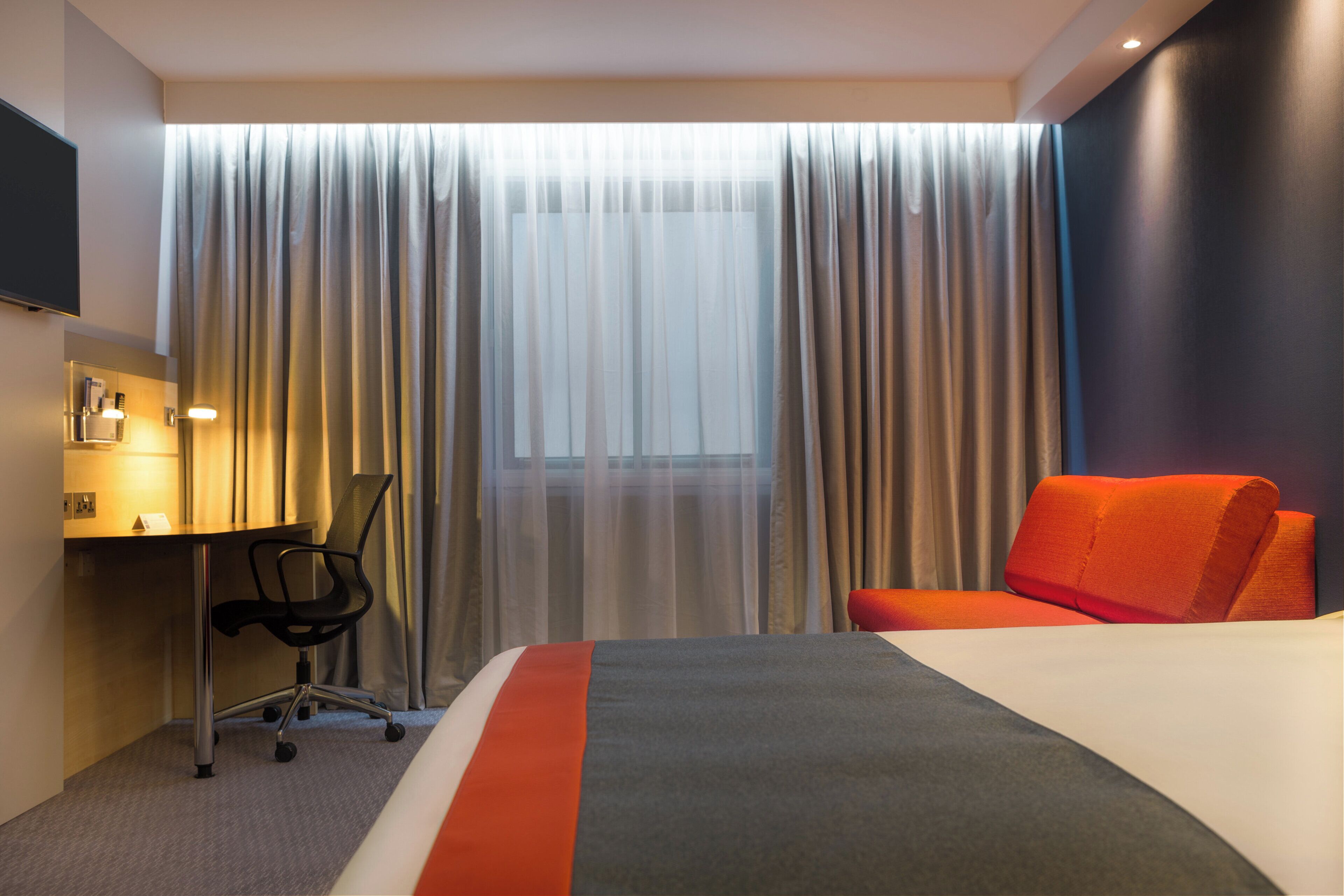 A hotel room with a bed, a desk, a chair, and a TV.