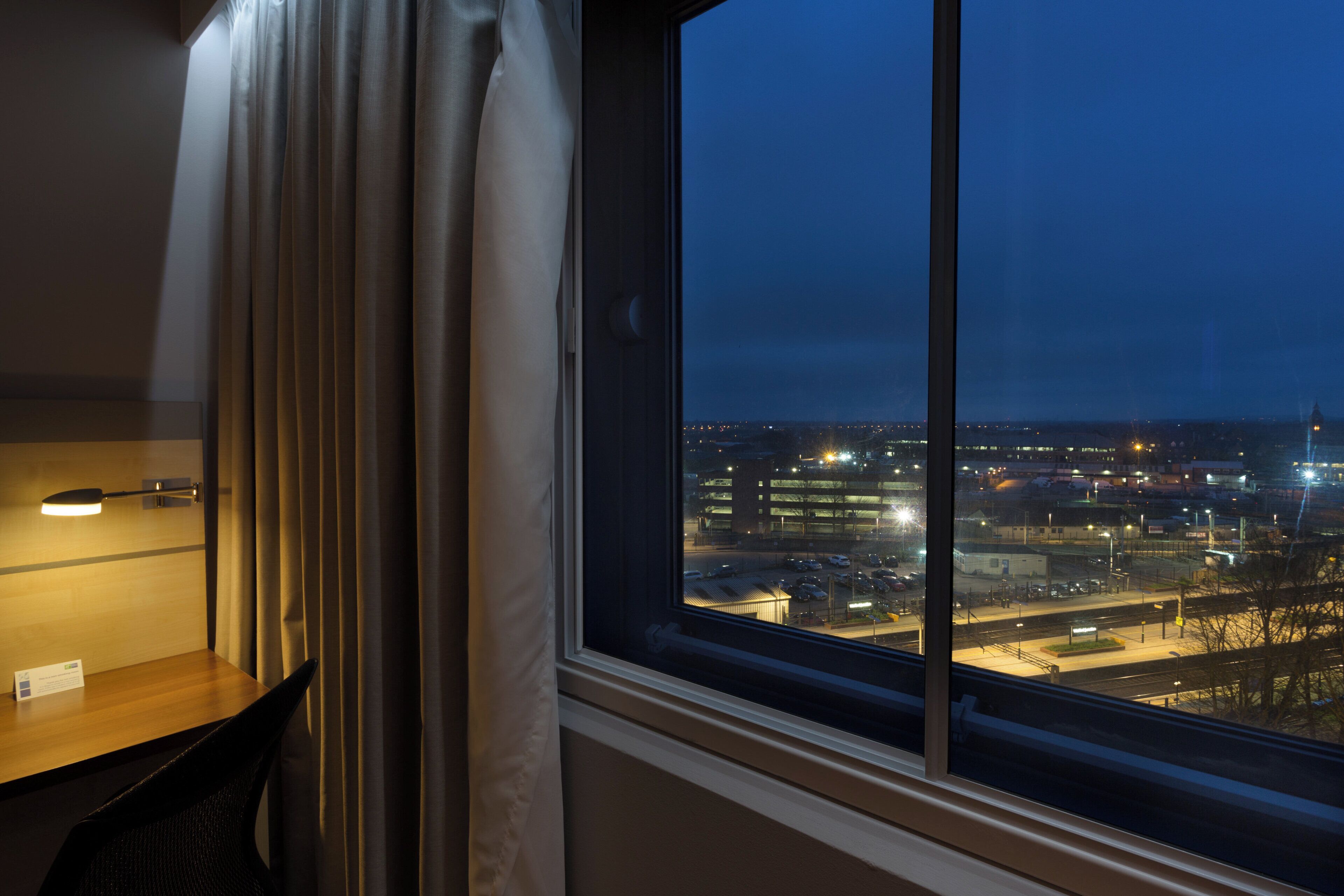 Habitación de hotel con un ventanal grande que da a una vista nocturna de la ciudad.