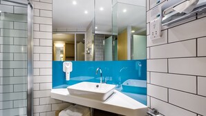 Ein modernes Badezimmer mit einem weißen Waschbecken, einer blauen Fliesenrückwand und einer Duschkabine aus Glas.