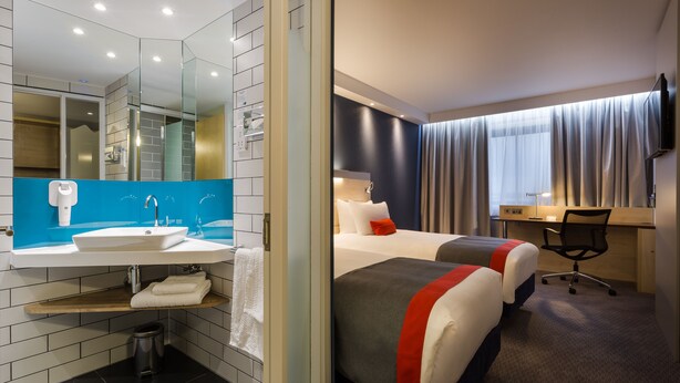 Ein Hotelzimmer mit Bad, Bett, Schreibtisch und Fernseher.