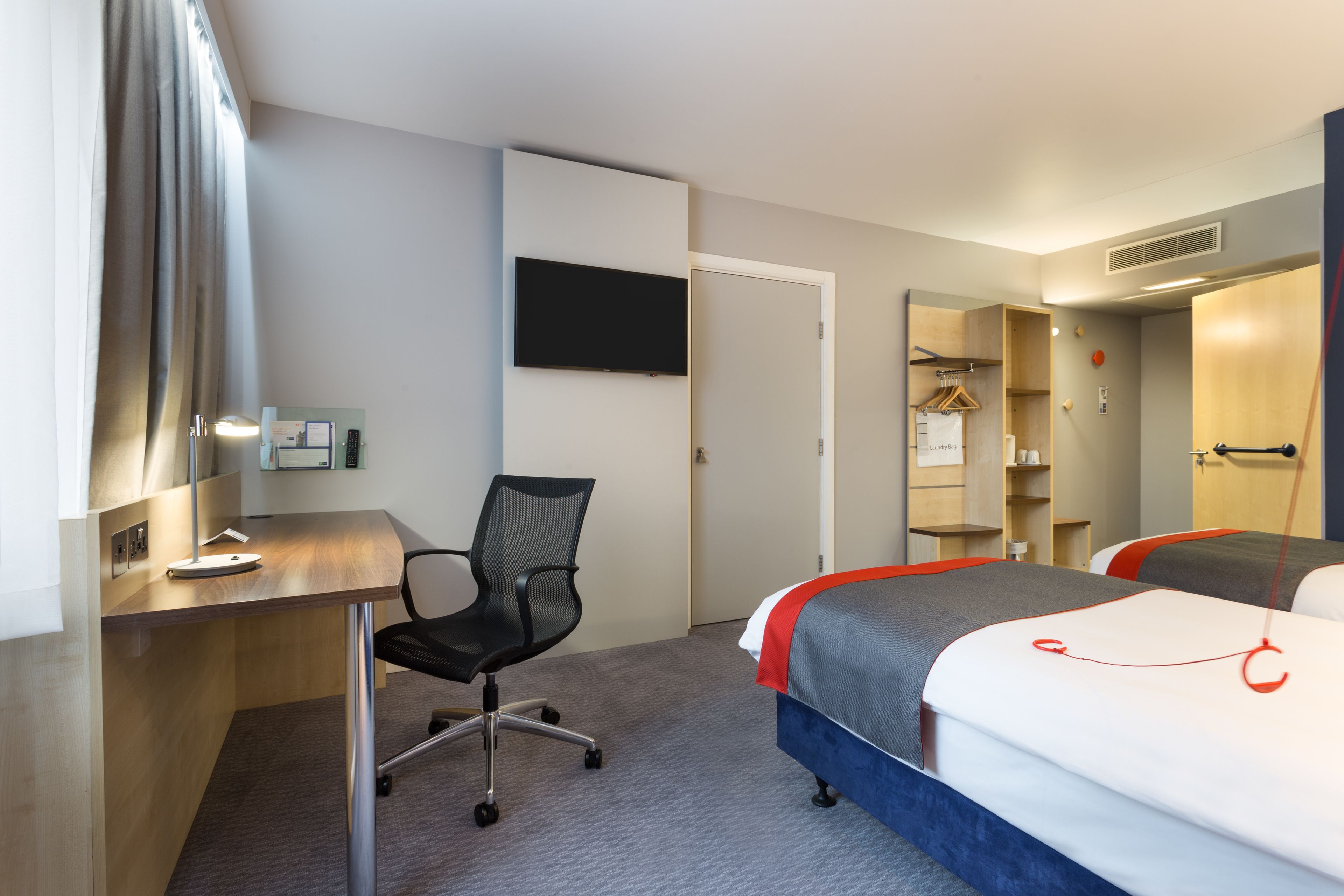 A hotel room with a desk, chair, two beds, a TV, and a wardrobe.